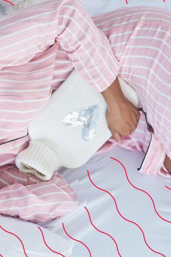 Femme en pyjama rose avec une bouillotte contre le ventre